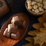 Chocolate truffles on a wooden plate with a basket of nuts and a bottle in the background.