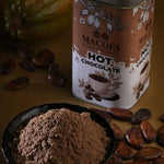 Macofa hot chocolate powder with cocoa powder and cacao beans on a wooden surface