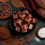 Chocolate truffles on a dark plate with cocoa beans, cacao nibs, and white powder on a rustic surface.