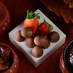 Chocolate truffles and strawberries on a white square plate with a dark background