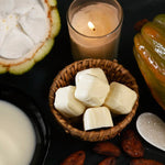 Cacao beans in a basket with a lit candle and cacao fruit on a dark surface